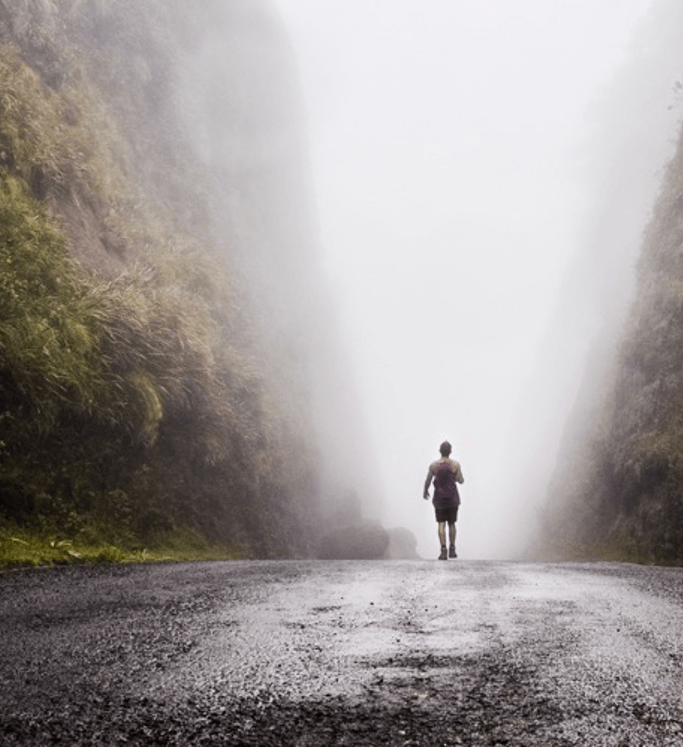 Stock photo of a person hikiing along a damp, foggy, valley path.