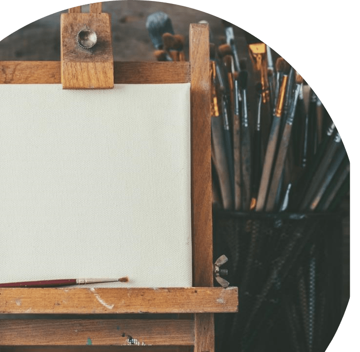 Stock image of an easel with a bundle of paint brushes beside it.