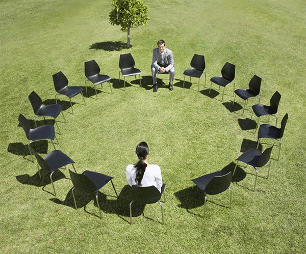 A stock photo of a circle of chairs in a field being occupied by only two people.
