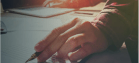 Stock photo of a hand with a pen resting on paper.